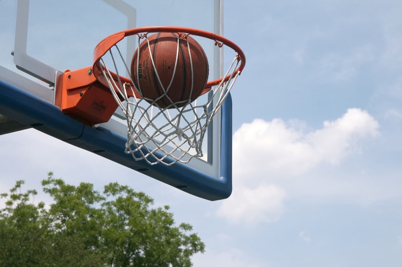 Basketball dropping through an outdoor hoop.