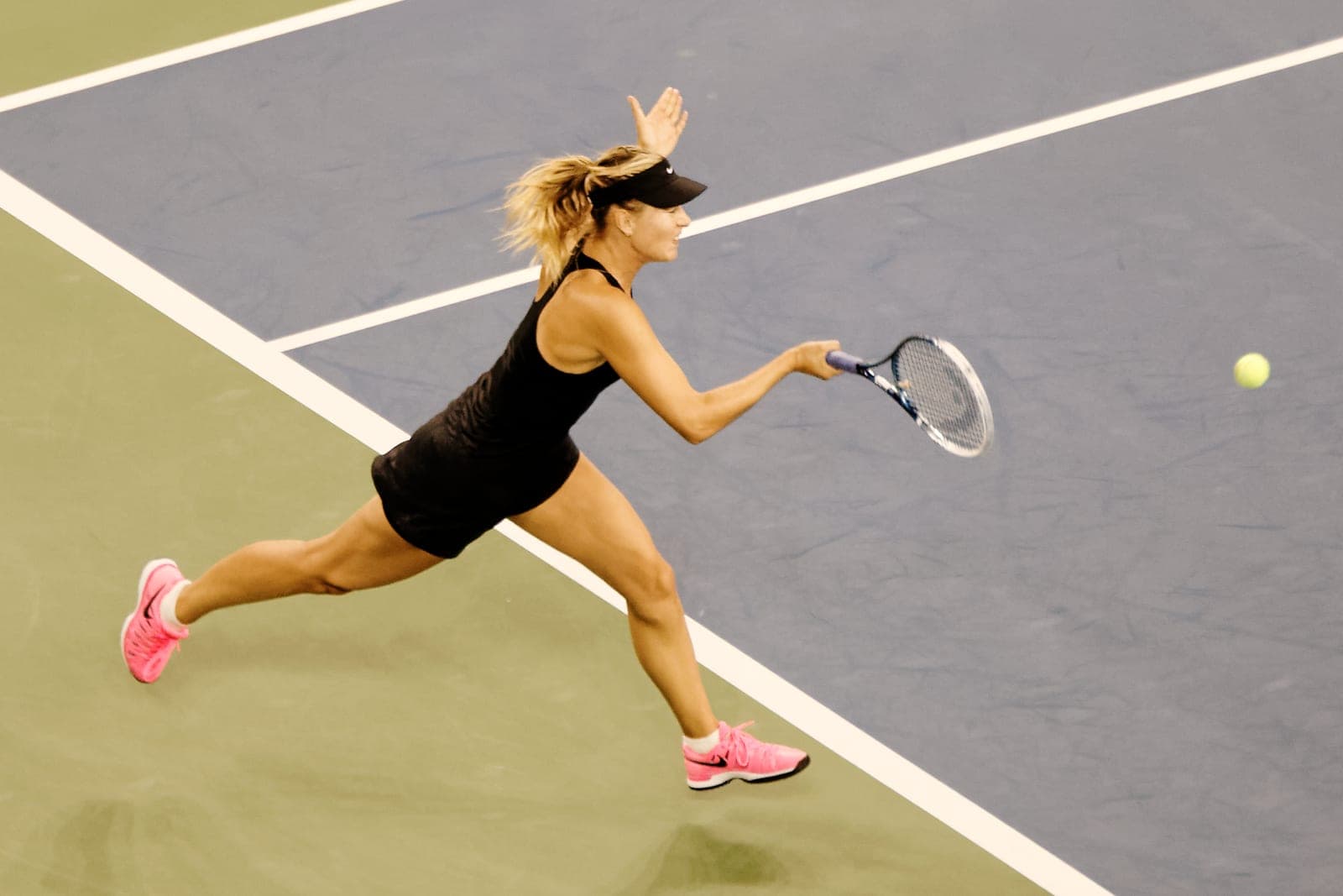 A tennis player lunges to hit a forehand on a hard court during a match.