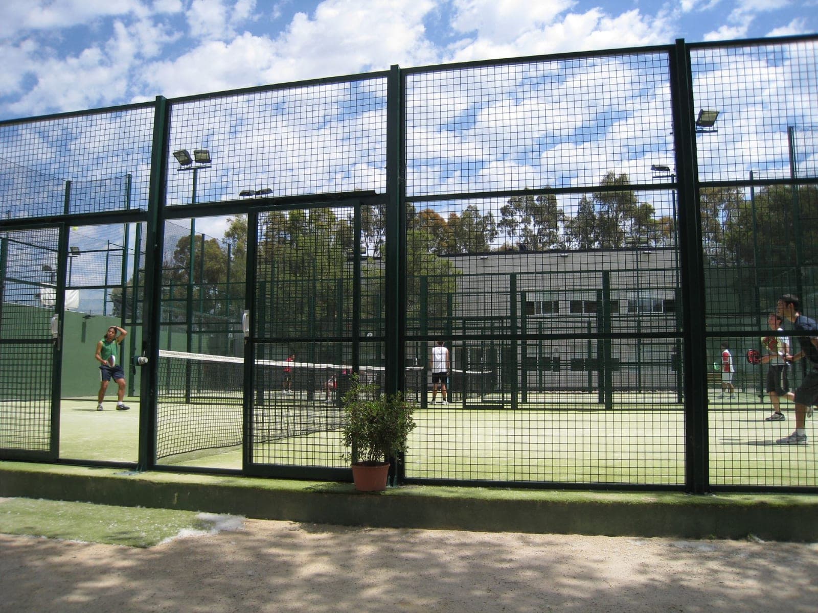 Players in a match on an enclosed, glass-walled padel court.