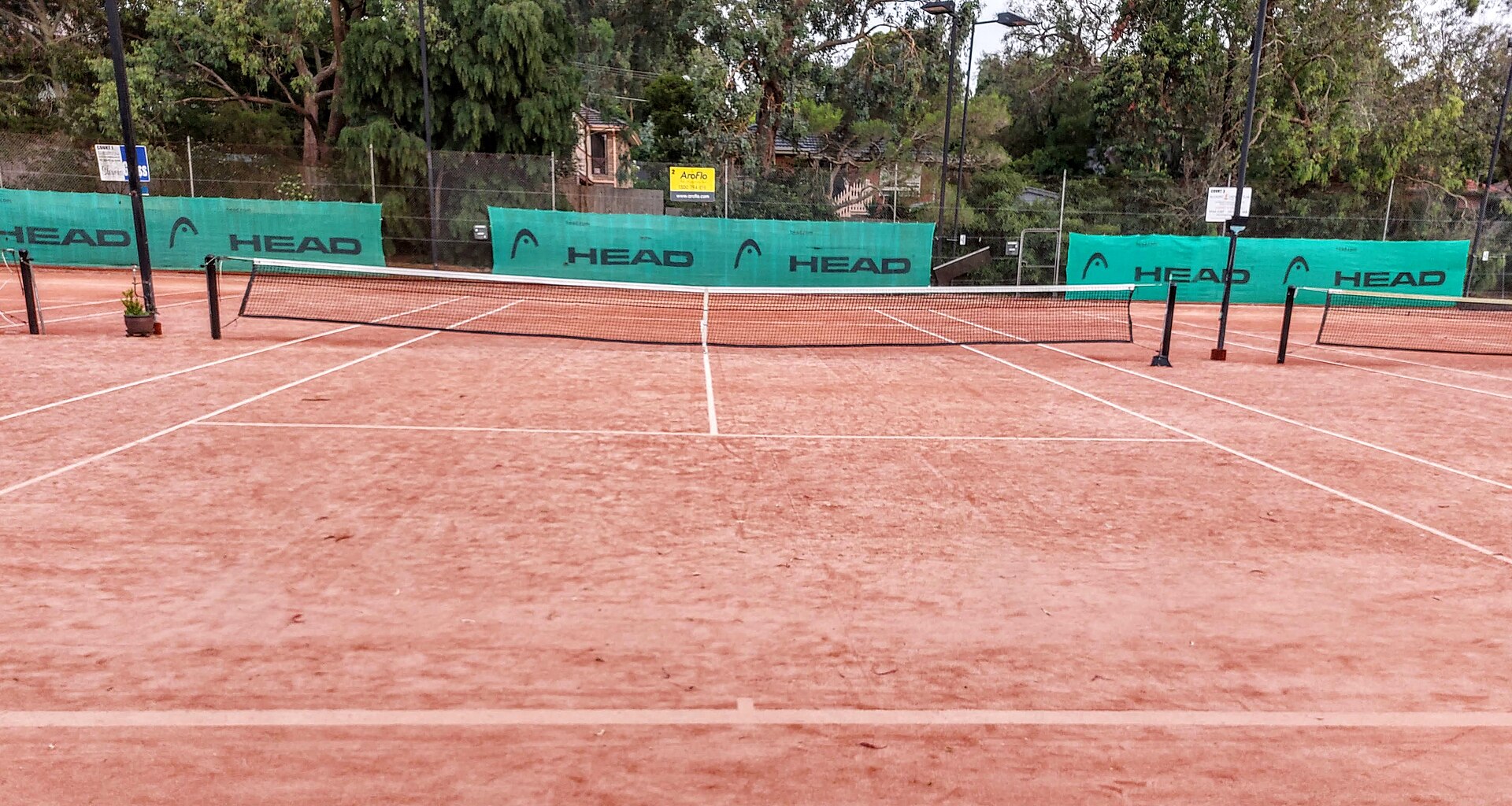 An empty red clay tennis court photographed along the centre line, with the net in the middle distance.