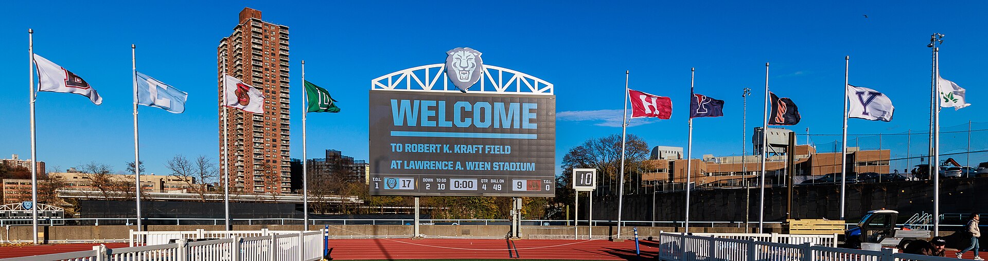A stadium scoreboard displaying a score and game clock, with flags mounted along the structure beside it.