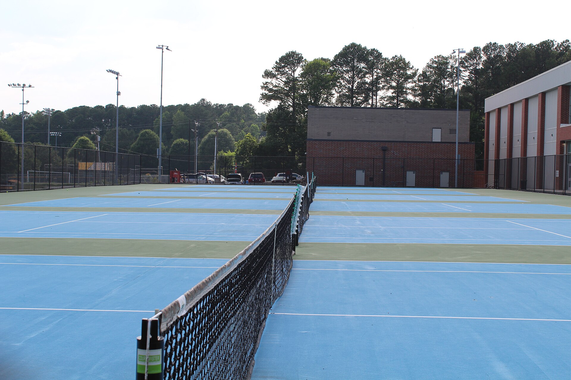 Blue and green outdoor hard tennis courts with white lines and dark green fencing.